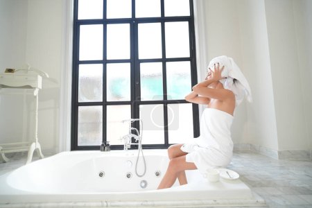 Foto de Concepto de higiene diaria. Hermosa mujer joven con toalla en el baño, feliz milenial disfrutando de la rutina de belleza de la mañana en casa - Imagen libre de derechos