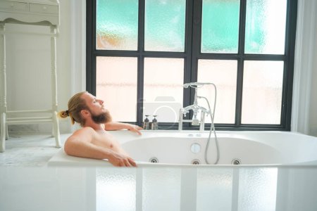 Photo for Relaxed young man bathing in modern bathroom luxury interior. Spa, wellness, body care concept - Royalty Free Image
