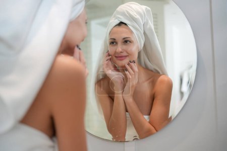 Téléchargez les photos : Concept de soins de la peau. Une femme regardant dans le miroir toucher le visage et la peau parfaite à la salle de bain. Focus sélectif - en image libre de droit