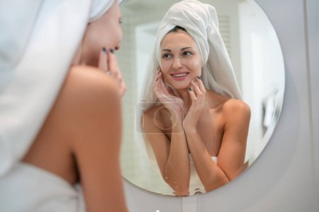 Photo for Skincare Concept. A Woman Looking In Mirror Touching Face And Perfect Skin At Bathroom. Selective Focus - Royalty Free Image