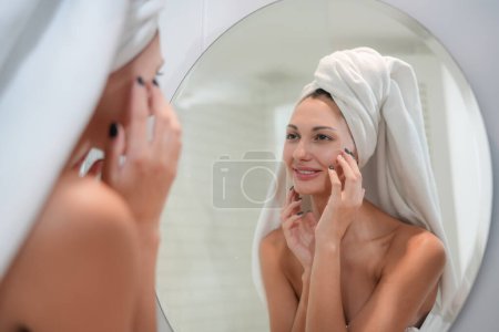 Téléchargez les photos : Concept de soins de la peau. Une femme regardant dans le miroir toucher le visage et la peau parfaite à la salle de bain. Focus sélectif - en image libre de droit