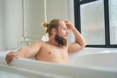 Photo for Relaxed young man bathing in modern bathroom luxury interior. Spa, wellness, body care concept - Royalty Free Image