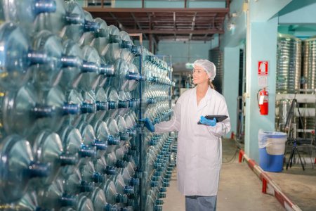Photo for Woman working at Reverse osmosis system for power plant. RO system for industry, equipment which popular to install with pipe at industrial such chemical, power plant, oil and gas. Young female worker in bottling factory checking water bottles - Royalty Free Image