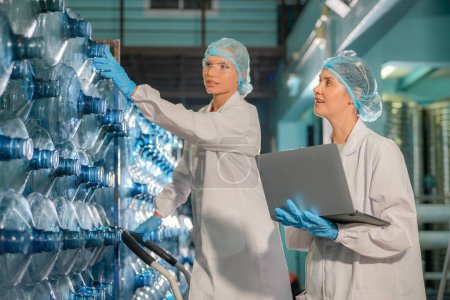 Photo for Women working at Reverse osmosis system for power plant. RO system for industry, equipment which popular to install with pipe at industrial such chemical, power plant, oil and gas. Young female workers in bottling factory checking water bottles - Royalty Free Image