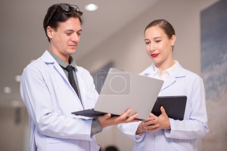 Téléchargez les photos : Tournage de deux jeunes médecins utilisant un ordinateur portable et discutant dans un bureau moderne - en image libre de droit
