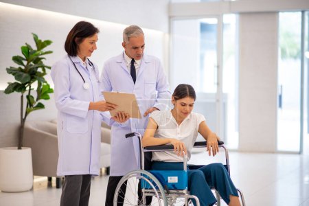 Foto de Médicos hablando con una paciente sentada en silla de ruedas. - Imagen libre de derechos