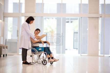 Téléchargez les photos : Médecin parlant avec une patiente assise sur un fauteuil roulant. - en image libre de droit