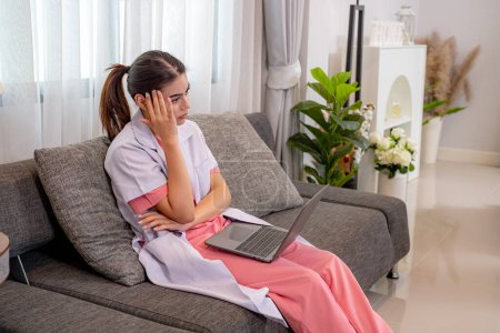 Foto de Enfermera atractiva en uniforme sentado en el sofá y el uso de ordenador portátil - Imagen libre de derechos