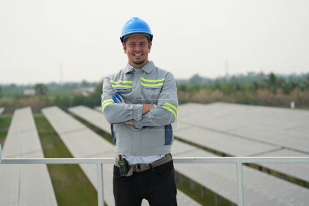 Téléchargez les photos : Ingénieur électricien avec casque travaillant dans une ferme photovoltaïque, équipement de contrôle et d'entretien avec des instruments à l'énergie solaire industrielle. - en image libre de droit