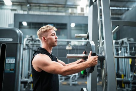 Foto de Atleta masculino haciendo ejercicio en el gimnasio, levantando pesas, tirando de las articulaciones. - Imagen libre de derechos