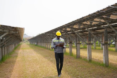 Téléchargez les photos : Ingénieur électricien avec casque blanc travaillant dans une ferme photovoltaïque, équipement de contrôle et d'entretien avec des instruments à l'énergie solaire industrielle. - en image libre de droit