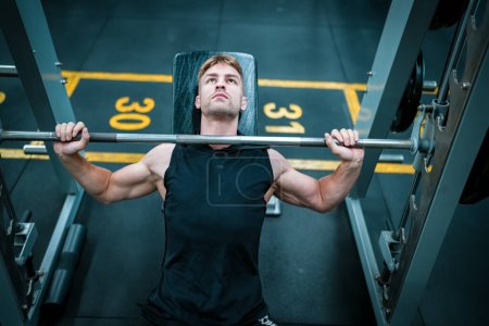 Foto de Atleta masculino haciendo ejercicio en el gimnasio, levantando pesas, tirando de las articulaciones. - Imagen libre de derechos