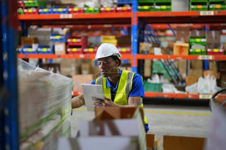 Photo for Worker working in large warehouse. checking boxes wrapped with plastic  on wooden pallet ready to ship to customer - Royalty Free Image