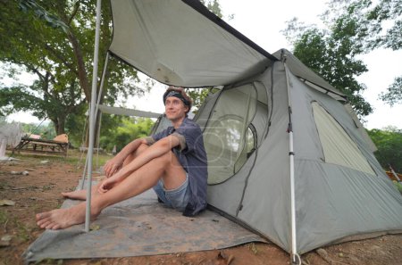 Foto de Joven turista masculino descansando cerca de la tienda en el campamento - Imagen libre de derechos