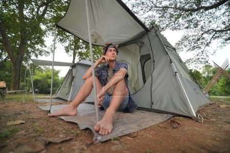 Foto de Joven turista masculino descansando cerca de la tienda en el campamento - Imagen libre de derechos