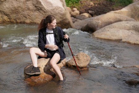 Téléchargez les photos : Aventure, voyage, tourisme, randonnée et concept de personnes. jeune femme avec des sacs à dos assis sur le rocher dans la rivière - en image libre de droit
