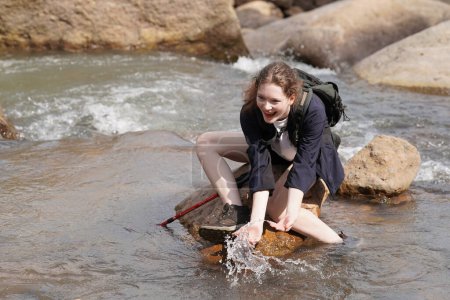 Foto de Aventura, viajes, turismo, senderismo y concepto de personas. joven mujer con mochilas sentado en la roca en el río - Imagen libre de derechos