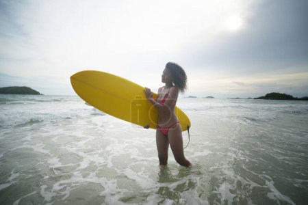 Téléchargez les photos : Jeune femme porte planche de surf dans les vagues douces - en image libre de droit