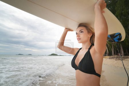 Foto de Mujer sexy posa con tabla de surf en la playa. mujer cargando sobre su tabla de surf de la cabeza en la puesta del sol - Imagen libre de derechos