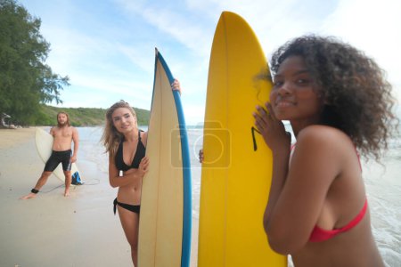 Photo for Young women and man surfers enjoying their time at the beach - Royalty Free Image