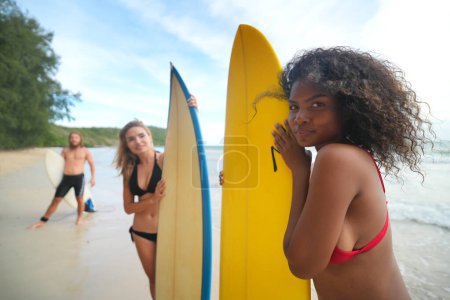 Photo for Young women and man surfers enjoying their time at the beach - Royalty Free Image
