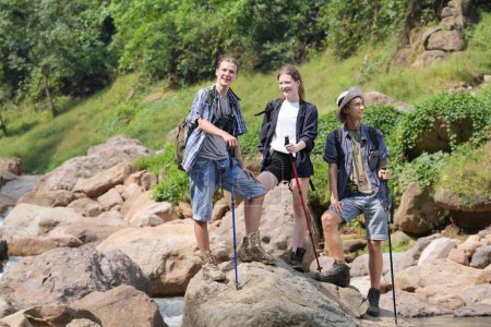 Photo for Hikers walking along a trail on a mountain with hiking sticks. Adventure, travel, tourism, hike and people concept. Group of smiling friends with backpacks outdoors. - Royalty Free Image
