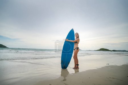 Photo for Mature woman carries surfboard into gentle waves - Royalty Free Image