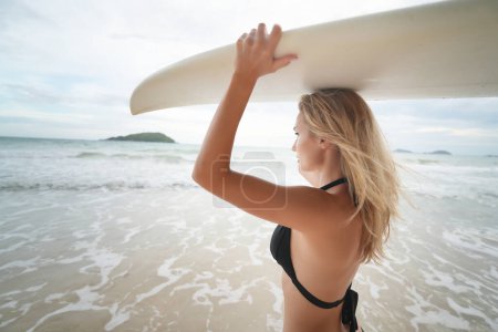 Foto de Mujeres sexy posa con tabla de surf en la playa. mujer cargando sobre su tabla de surf de la cabeza en la puesta del sol - Imagen libre de derechos