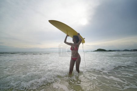 Téléchargez les photos : Jeunes femmes métisses profitant de leur temps à la plage, tenant des planches de surf - en image libre de droit