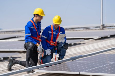 Téléchargez les photos : Ingénieurs professionnels vérifiant le toit solaire sur le toit de l'usine sous la lumière du soleil. Ingénieurs ayant un emploi de service d'énergie électrique renouvelable - en image libre de droit