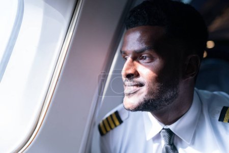 Téléchargez les photos : Heureux jeune pilote en uniforme professionnel à l'aéroport. Pilote assis dans le cockpit de l'avion - en image libre de droit