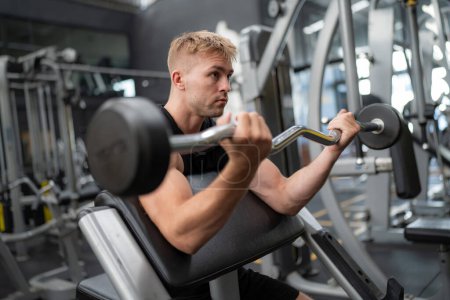 Photo for Young handsome fit man in gym working out, lifting barbell - Royalty Free Image
