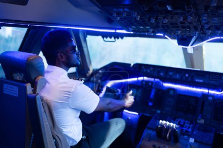 Foto de Feliz joven piloto en uniforme profesional en el aeropuerto. Piloto masculino sentado en la cabina del avión - Imagen libre de derechos