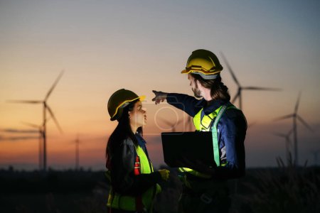 Téléchargez les photos : Deux ouvriers industriels multiraciaux examinant des éoliennes. Zone rurale avec éco-ferme de production énergie verte propre - en image libre de droit