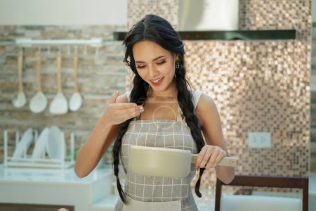 Foto de Atractiva joven cocinera en la cocina doméstica - Imagen libre de derechos