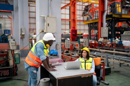 Foto de Equipo de técnicos que usan cascos de protección que estudian el manual de operación mientras están de pie en la unidad de máquina CNC - Imagen libre de derechos