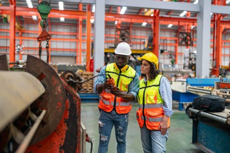 Foto de Dos técnicos altamente profesionales que usan overoles y sombreros en el departamento de producción de la planta moderna y discuten ideas - Imagen libre de derechos