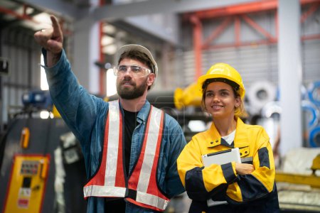 Foto de Jóvenes técnicos exitosos de máquinas industriales en cascos de seguridad y ropa de trabajo de pie en un gran garaje o taller - Imagen libre de derechos