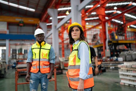 Foto de Dos técnicos altamente profesionales que usan overoles y sombreros en el departamento de producción de la planta moderna y discuten ideas - Imagen libre de derechos