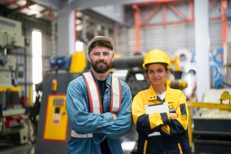 Photo for Young successful technicians of industrial machines in safety helmets and workwear standing in large garage or workshop - Royalty Free Image