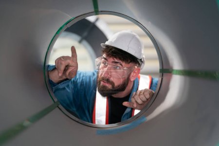 Téléchargez les photos : Portrait de l'ingénieur masculin examinant la qualité des tuyaux en acier métallique en regardant à l'intérieur du tube à l'entrepôt de l'usine. - en image libre de droit