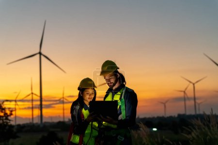 Foto de Dos trabajadores industriales multirraciales que examinan turbinas eólicas. Zona rural con eco explotación de producción energía verde limpia - Imagen libre de derechos
