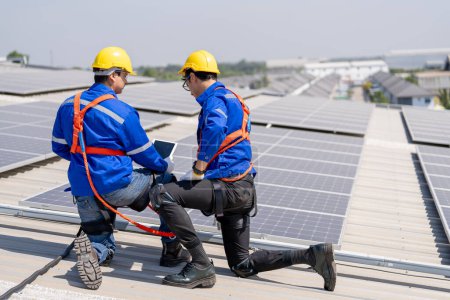 Téléchargez les photos : Ingénieurs professionnels vérifiant le toit solaire sur le toit de l'usine sous la lumière du soleil. Ingénieurs ayant un emploi de service d'énergie électrique renouvelable - en image libre de droit