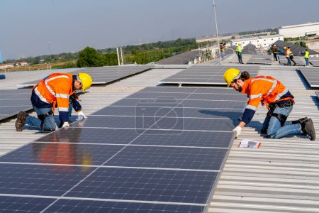 Téléchargez les photos : Ingénieurs professionnels vérifiant le toit solaire sur le toit de l'usine sous la lumière du soleil. Ingénieurs ayant un emploi de service d'énergie électrique renouvelable éco - en image libre de droit