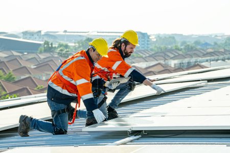 Téléchargez les photos : Ingénieurs professionnels vérifiant le toit solaire sur le toit de l'usine sous la lumière du soleil. Ingénieurs ayant un emploi de service d'énergie électrique renouvelable éco - en image libre de droit