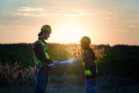 Foto de Dos trabajadores industriales multirraciales que examinan turbinas eólicas. Zona rural con eco explotación de producción energía verde limpia - Imagen libre de derechos