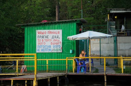 Photo for Boat station on the pond, wooden berth, woman manager smoking under tent waiting for clients. May 12, 2021. Pushcha Vodytsia park, Kyiv, Ukraine - Royalty Free Image