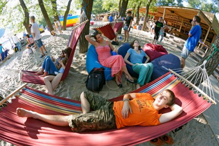 Foto de Hombre relajándose en una hamaca, mujeres sentadas en bolsas de frijoles, acampando en una playa de arena. Fest Vedalife. 25 de julio de 2018. Kiev, Ucrania - Imagen libre de derechos
