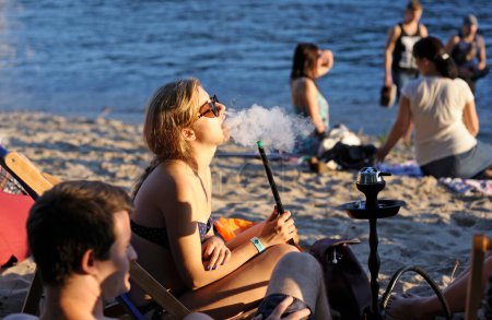 Photo for Girl sitting on a beach and smoking a hookah, people on a background. Fest Vedalife. July 25, 2018. Kyiv, Ukraine - Royalty Free Image