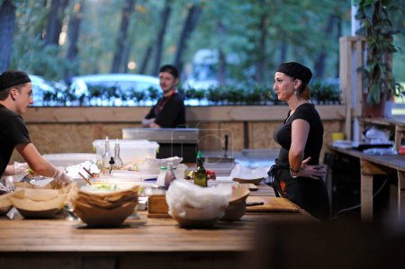 Foto de Cocina comunicándose mientras prepara comidas de comida rápida en una cocina de un restaurante. Fest Vedalife. 25 de julio de 2018. Kiev, Ucrania - Imagen libre de derechos